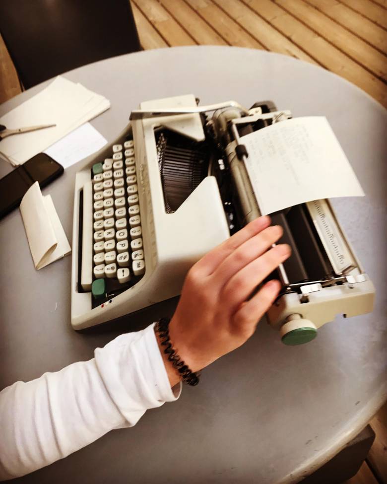 A hand works on a typewriter on a table.