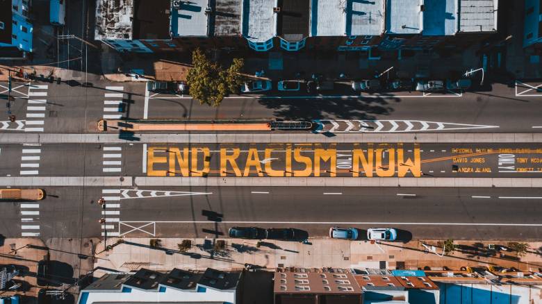 Birds Eye view of a road that reads "END RACISM NOW" in large yellow painted block letters.