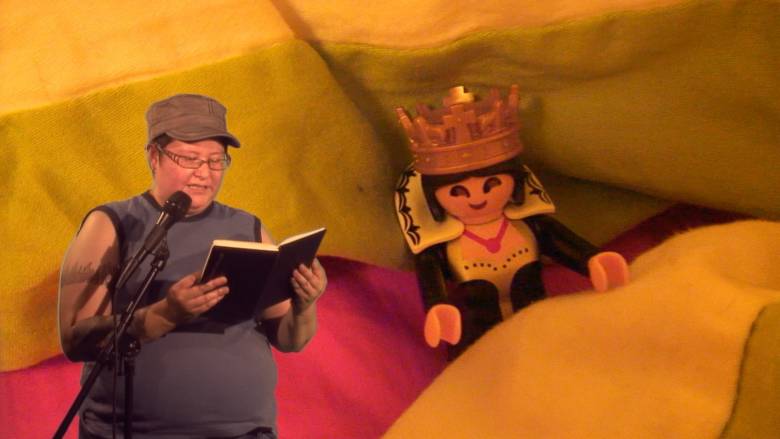 Thirza Jean Cuthand reading from a book on left of image with background of lego human with crown on