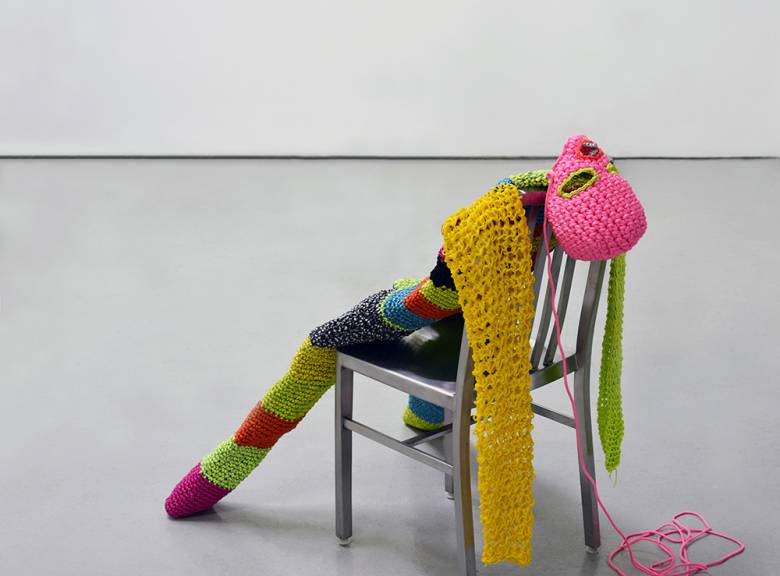 Image of brightly coloured crocheted person lying against chair