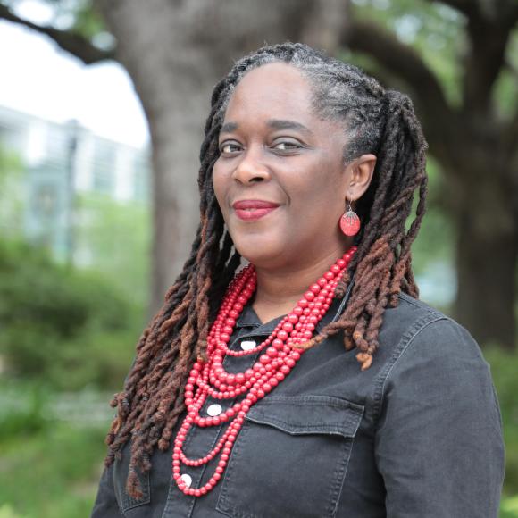 Black woman with long black/brown hair wearing a red necklance and black blouse