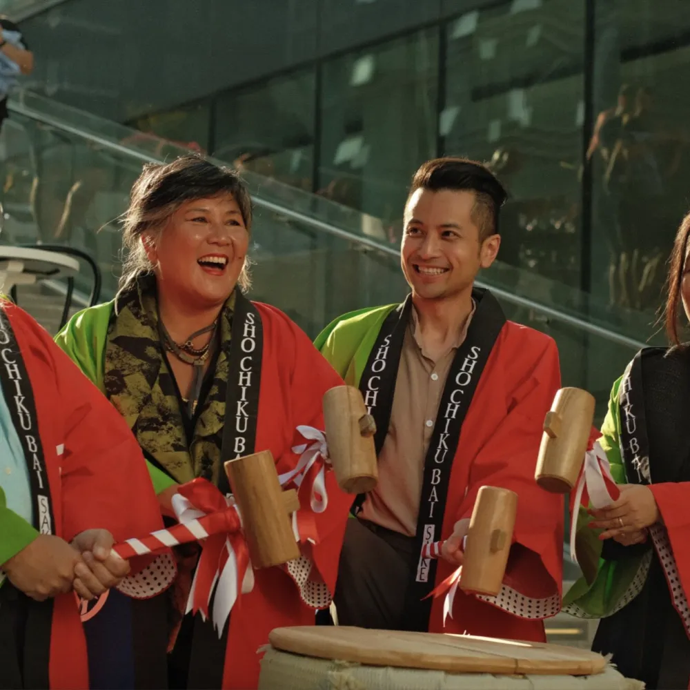 Four people in cultural adornment holding mallets over a drum.