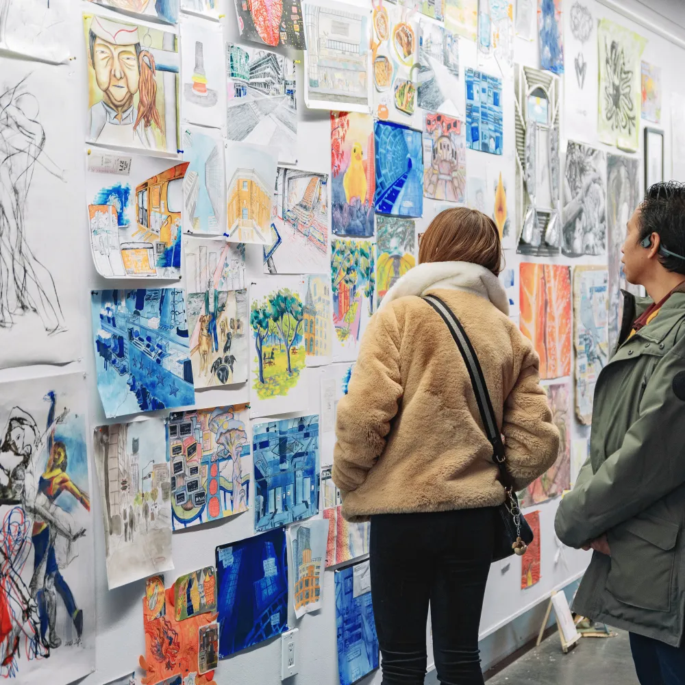 Two people standing in front of a gallery wall covered in artwork and sketches